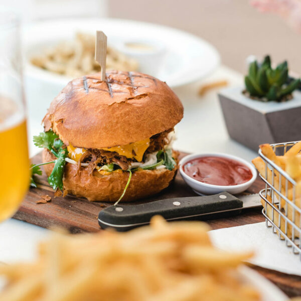 Restaurant table with plates of fries, glasses of beer, and huge hamburgers.