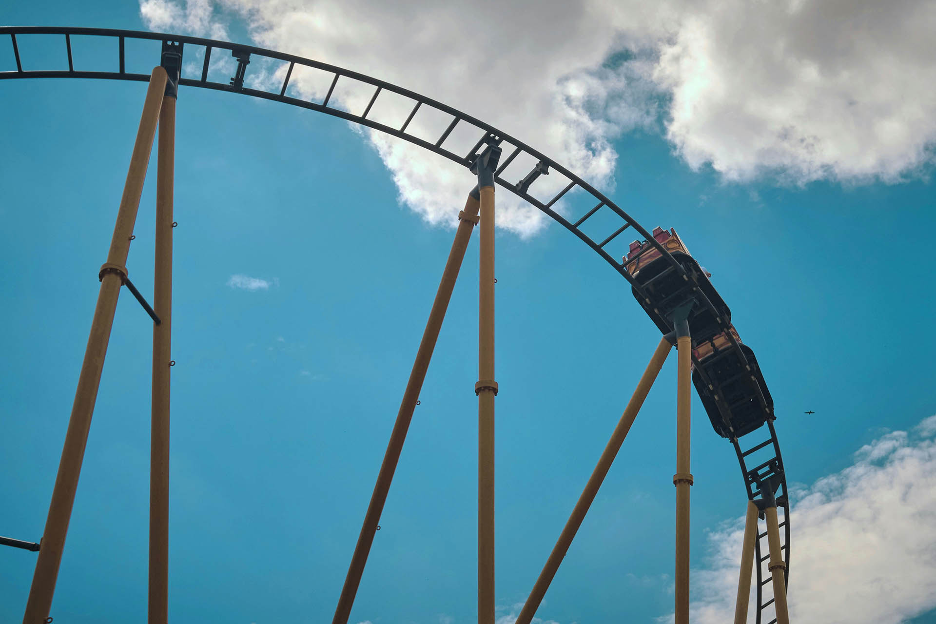 People riding on roller coaster under bright summer skies.